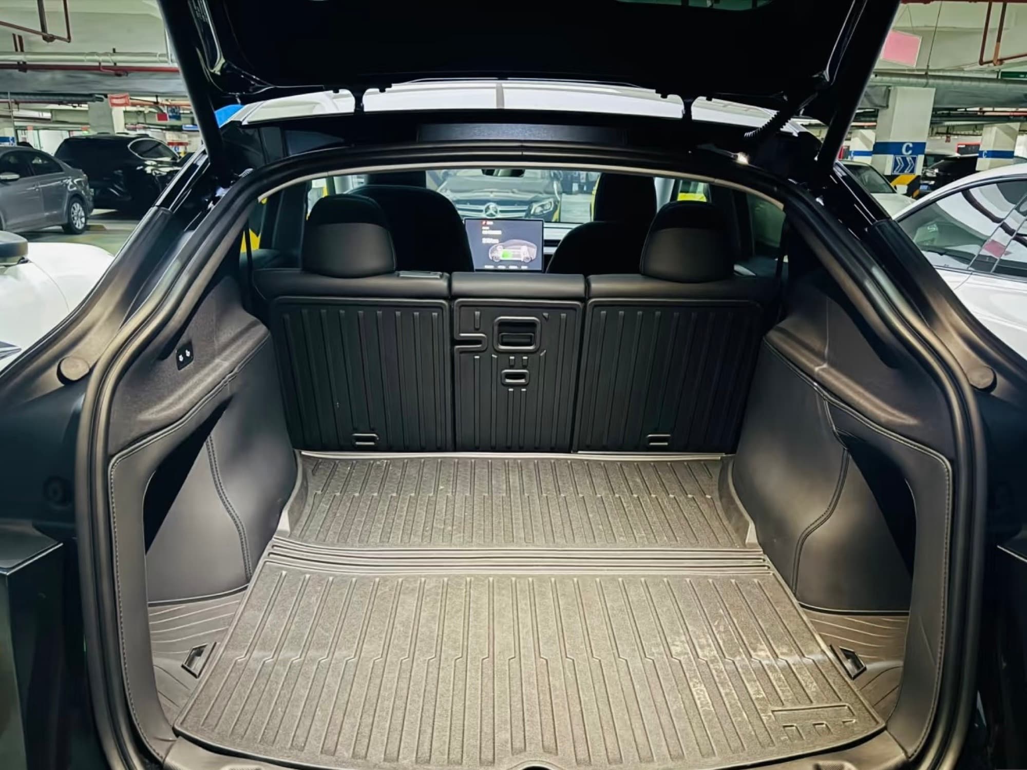 Open Model Y rear hatch showing the empty cargo floor, wheel housings, and upright rear seats