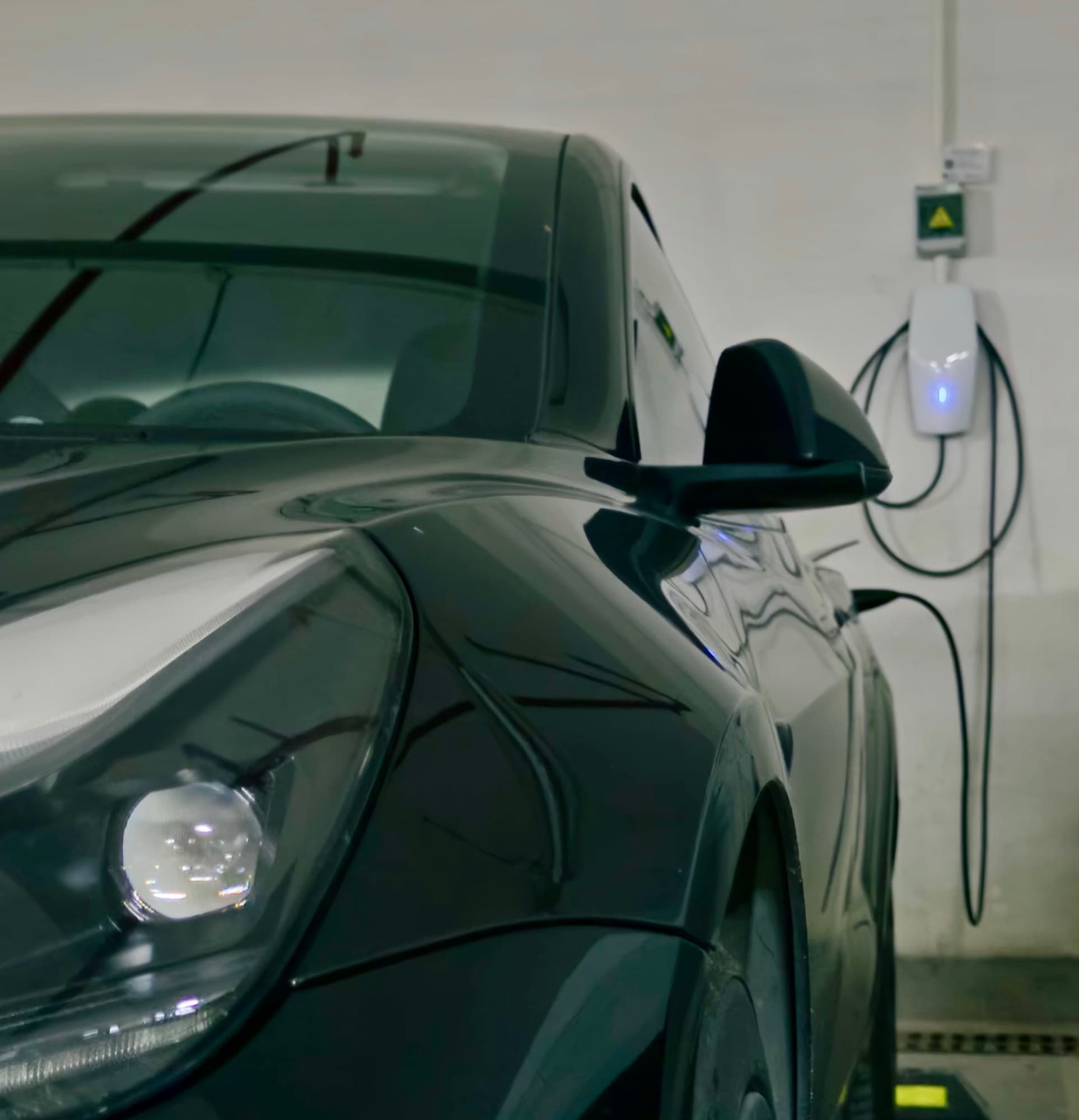 Model Y parked beside a wall charger with its cable connected and coiled on the wall