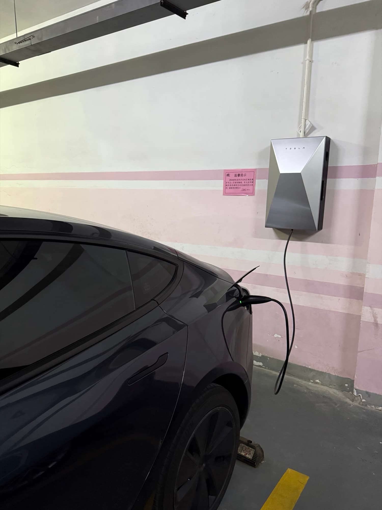 Dark Model Y connected to a wall-mounted Tesla charger in an indoor parking space