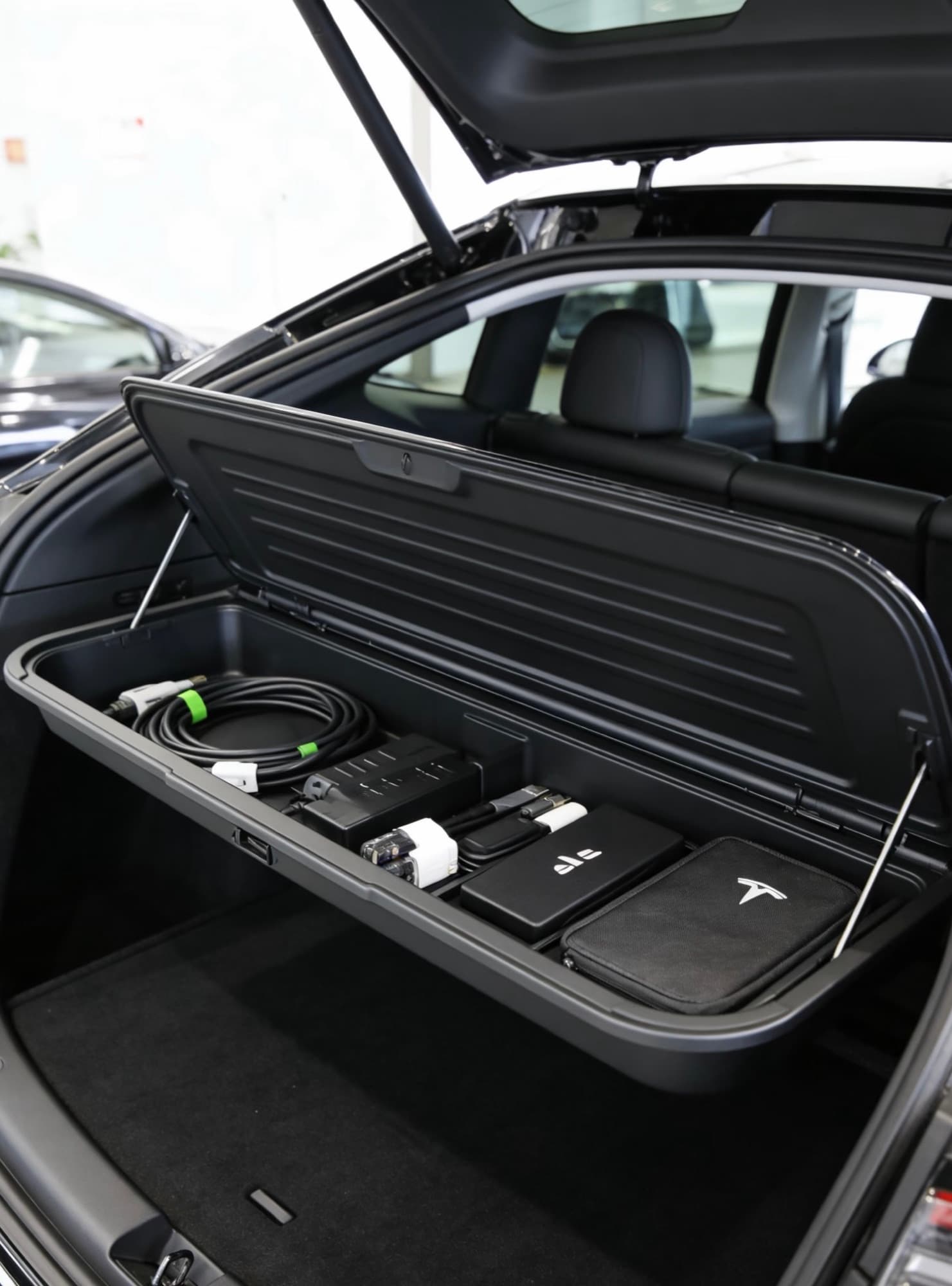 Raised trunk storage organizer holding charging cables and small accessories above a Model Y cargo floor