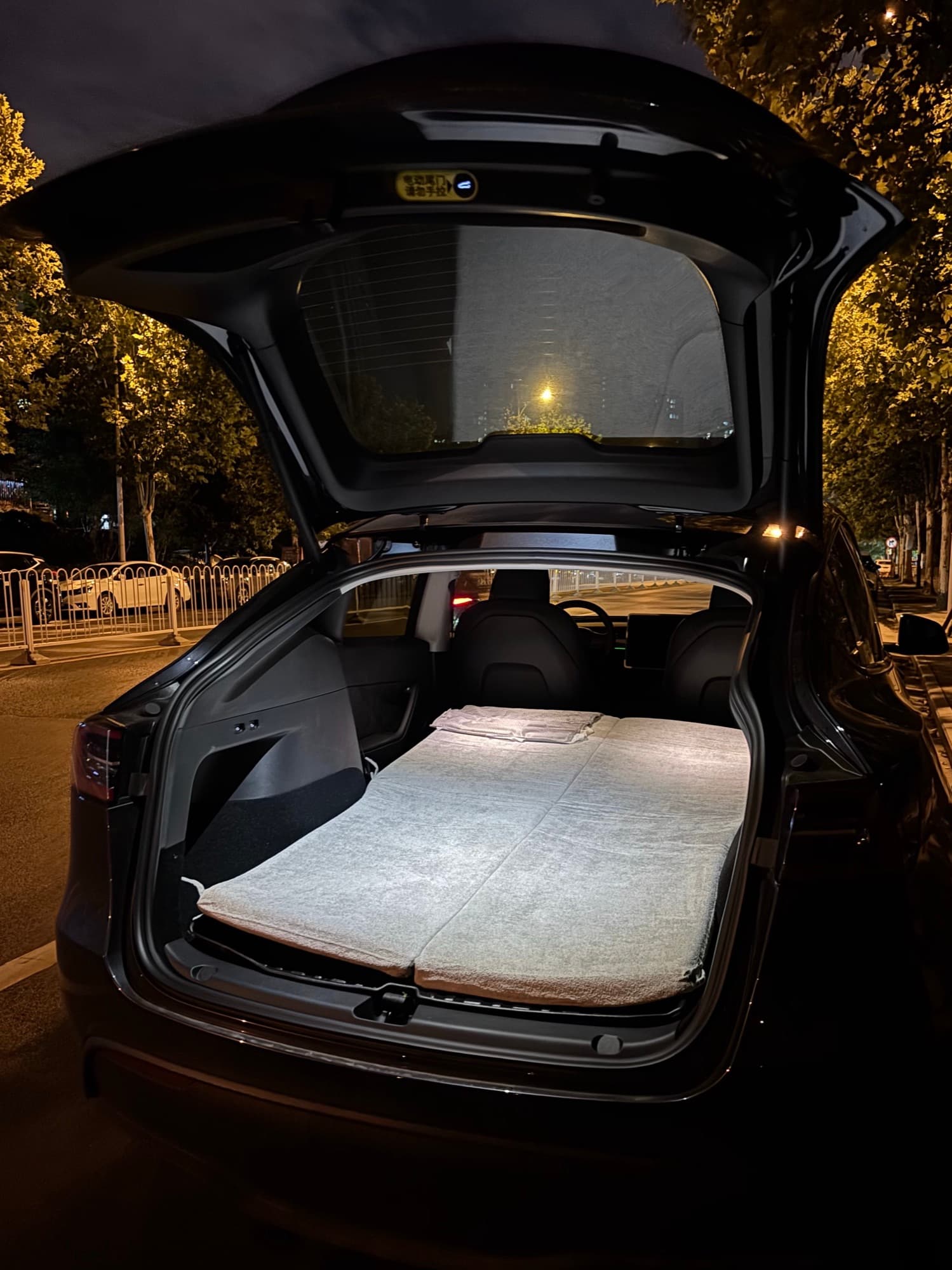 Gray fitted mattress covering the folded rear seating and cargo floor of a Model Y at night
