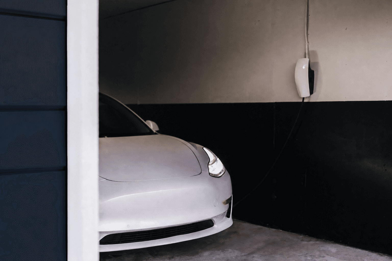 White electric car connected to a wall charger inside a residential garage